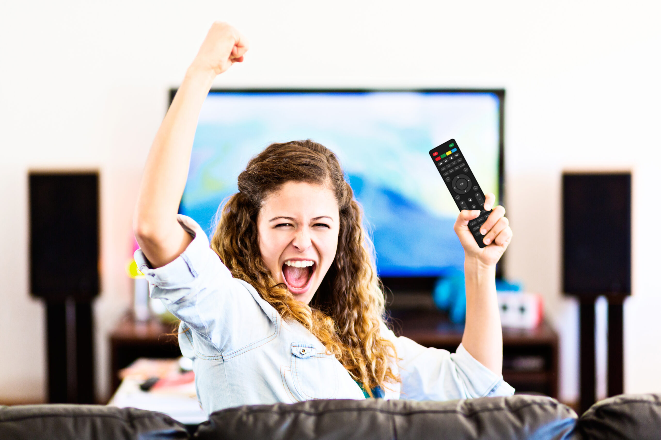 Enthusiastic young female spectator turns from TV cheering triumphantly